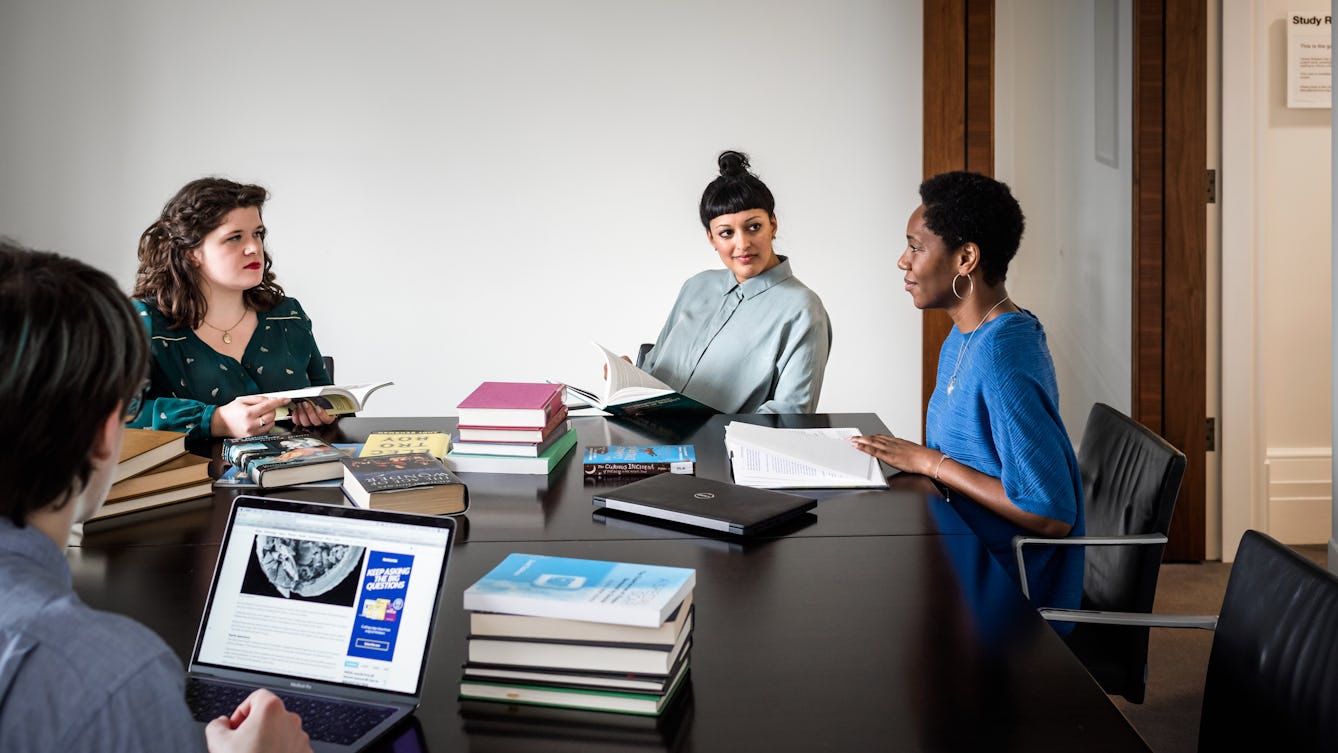 A group seated around a table with books and laptops in a study space.