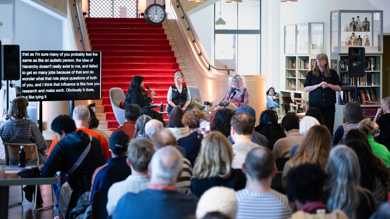 Photograph of a seated audience at an event in the Reading Room at Wellcome Collection. At the front of the room a panel of 3 speakers are seated facing the audience with microphones, a BSL translator is standing on the stage.