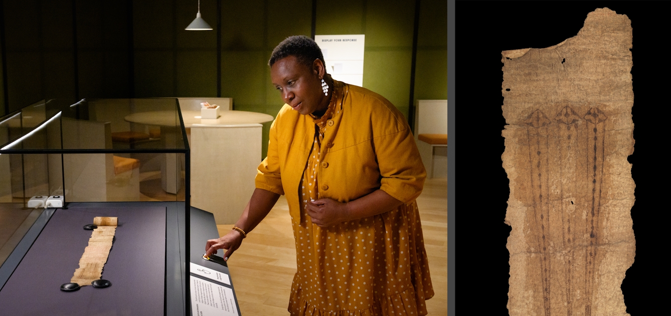 A visitor pushing a button and looking at a scroll, housed in glass display cases. 