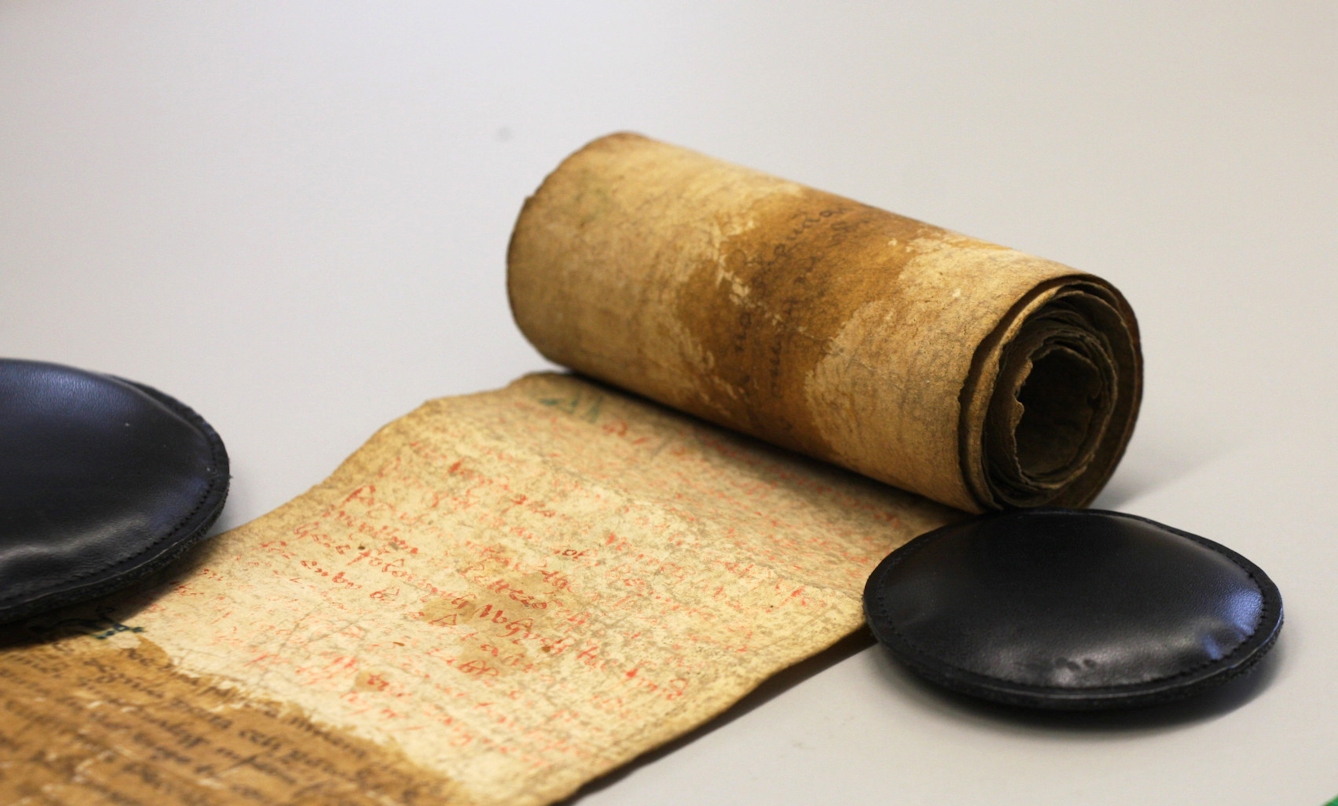 A Medieval rolled up parchment scroll with faded text and stains showing its age and fragility.