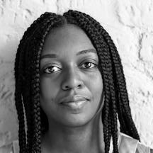 Balck and white photograph of the head and shoulders a young black woman with long braided hair. She is looking directly at the camera.
