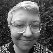 Black and white photograph of the head and shoulders of a young white person with short blonde hair and glasses. They are smiling and looking straight at the camera.