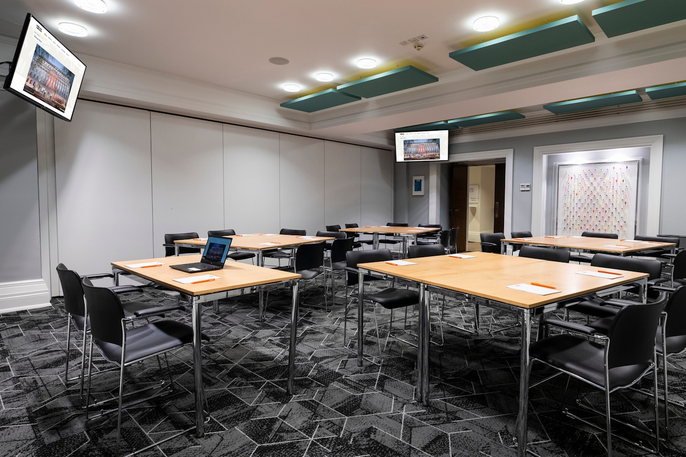 Flexible event space set up with tables and chairs arranged in small groups, with presentation screens.