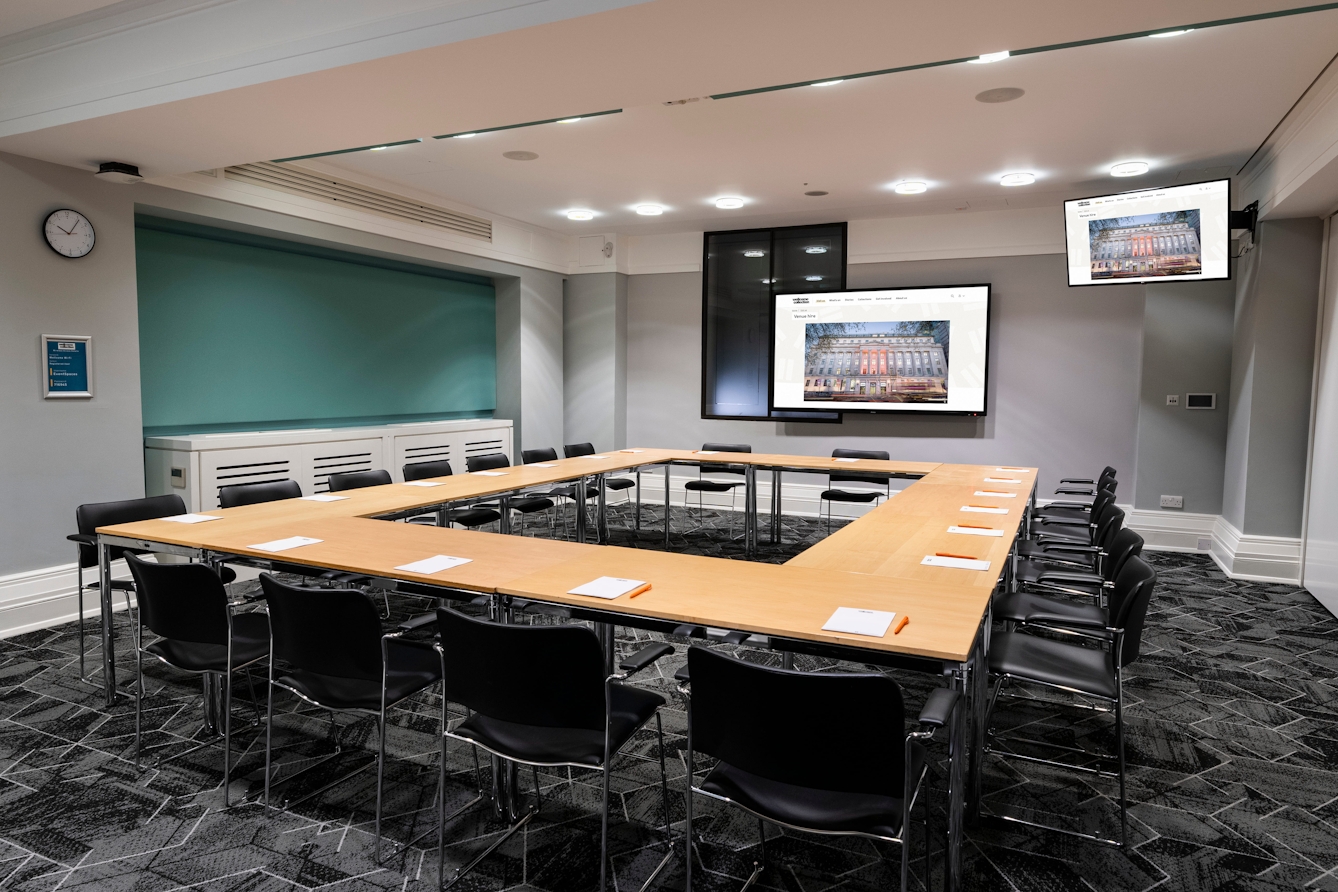 Flexible conference room set up with tables arranged in a large square, facing a presentation screen in a bright, modern meeting space.